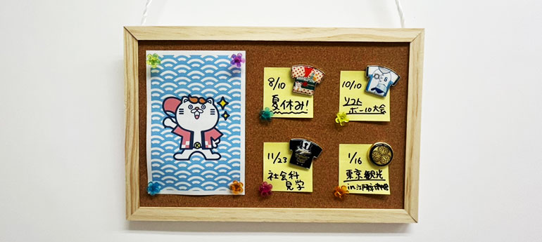 コルクボードに4つのピンバッジとポストカードが飾られている画像