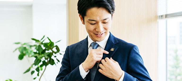 スーツ・ジャケットのフラワーホールに社章がしっかり付いているかを確認している男性のイメージ画像