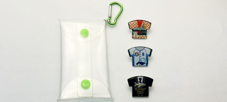 空のクリアポーチとシャツの形をした柄が異なる3種類のオリジナルピンバッジが縦に並んでいる画像