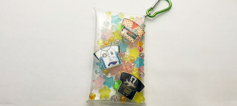 クリアポーチの中にシャツの形をした柄が異なる3種類のオリジナルピンバッジとカラフルなビーズを収納した画像