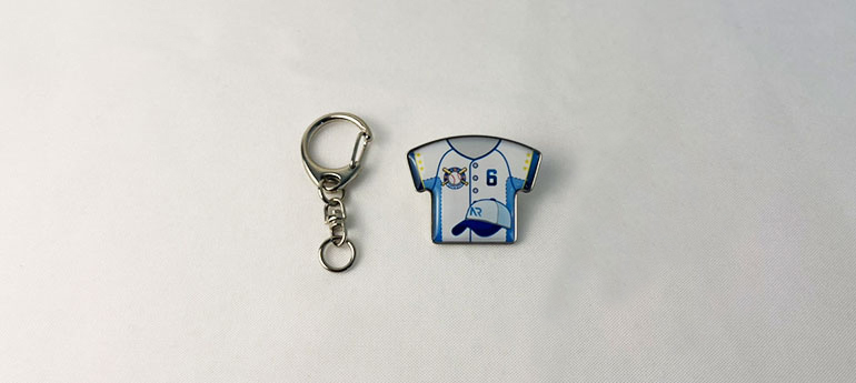 シルバーのキーホルダーパーツとシャツの形をしたオリジナルピンバッジが並んでいる画像