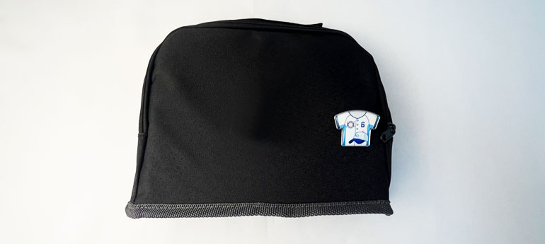 普段使用している黒色のジッパータイプのポーチの上に、シャツの形をしたオリジナルピンバッジが置いてある画像