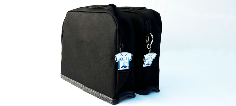 ジッパー部分にシャツの形をしたオリジナルピンバッジを直接取り付けた黒いポーチと、シャツの形をしたオリジナルピンバッジをナスカンタイプのキーホルダーパーツに装着したアイテムを、ジッパー部分に取りつけた黒いポーチが並んでいる画像