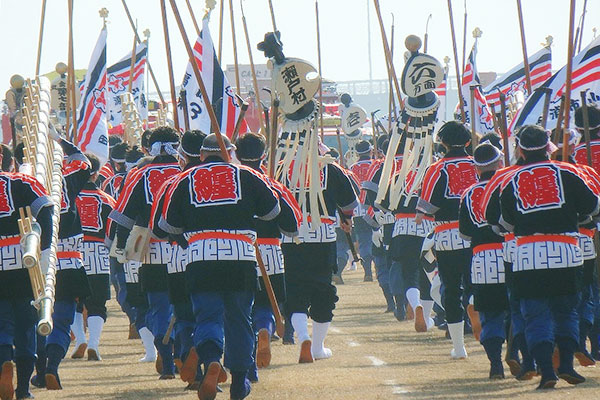 刺子半纏（消防法被）を着用し、纏や梯子を担いで集団で移動をしている現代の火消したちのイメージ画像
