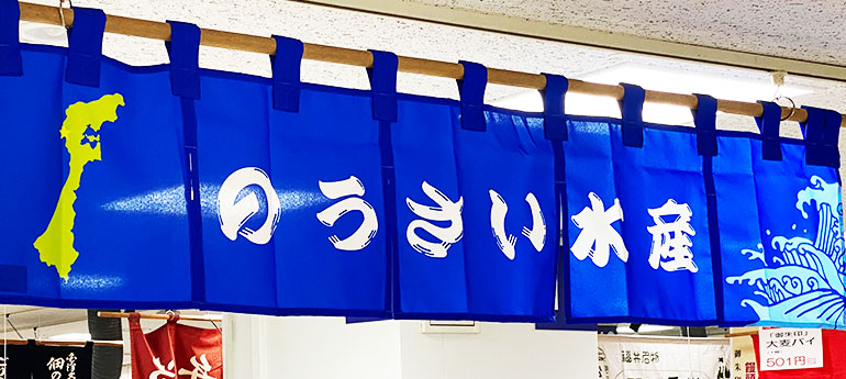 青色の生地に白い文字で「のうさい水産」と名入れ印刷されている他、緑色の地形のイラストと水色の高波のイラストもプリントされている、5巾のオリジナルのれんの実例画像