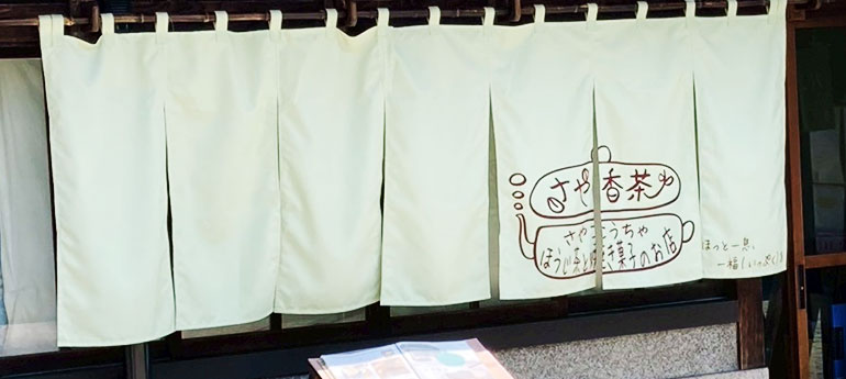 薄いモスグリーン色の生地の7巾のれんの、右端3巾にカフェの店名とオリジナルのイラストが名入れプリントされた、オリジナルのれんの実例画像