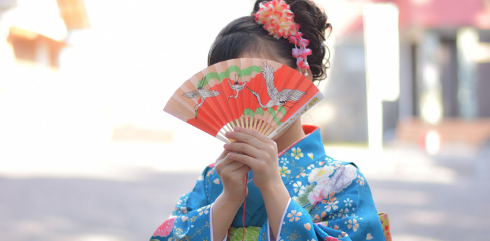 水色の着物を着た小さな女の子が顔の前で扇子を広げているイメージ画像