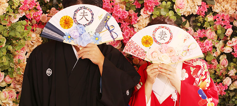 新郎新婦が結婚式の撮影用に、扇子の扇面にそれぞれ「夫」「妻」と名入れ印刷して製作した、オリジナル扇子を顔の前に掲げて記念撮影しているイメージ画像